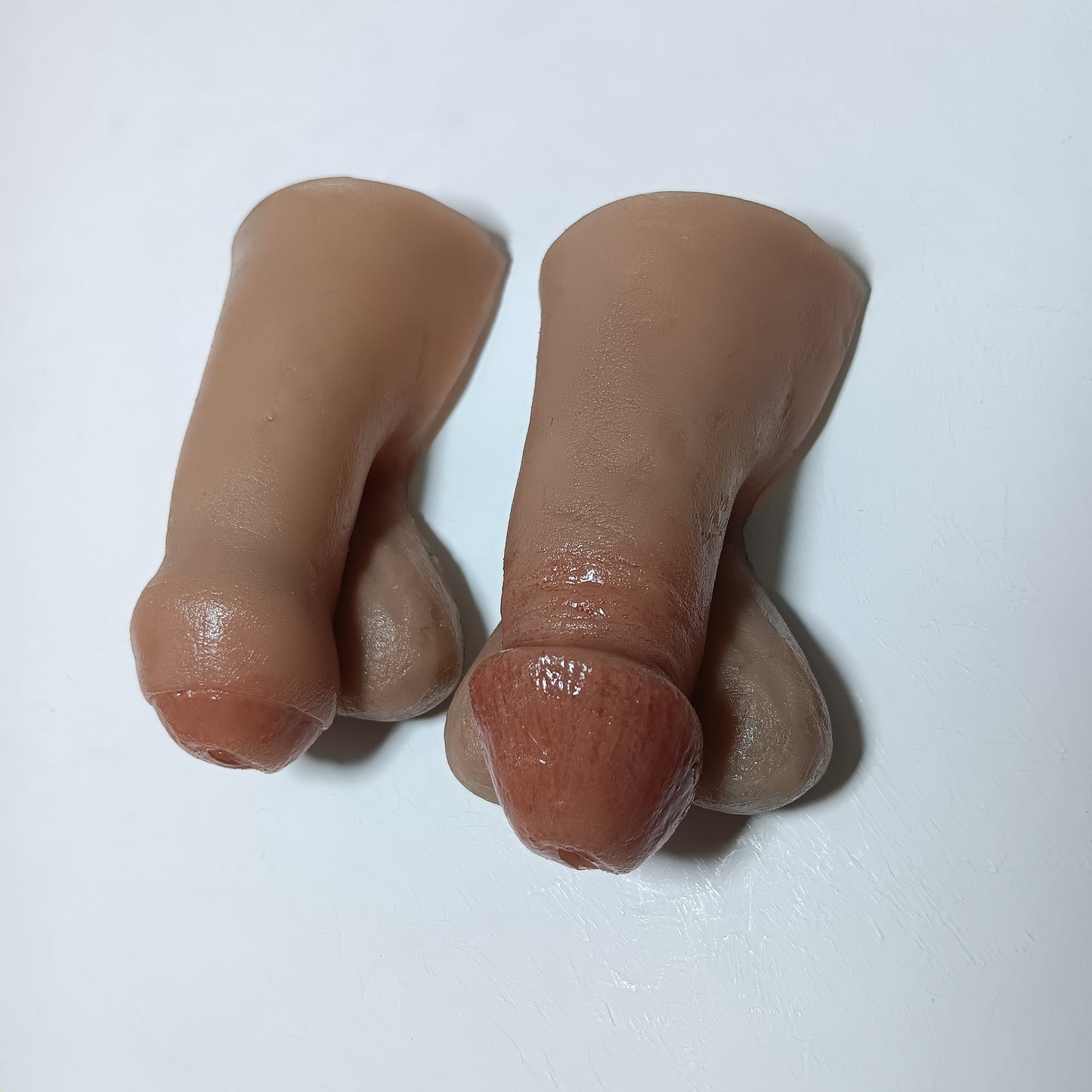 A photo showing two realistic finished 2 inch STP Skins with style options circumcised and uncircumcised lifelike silicone prosthetic.