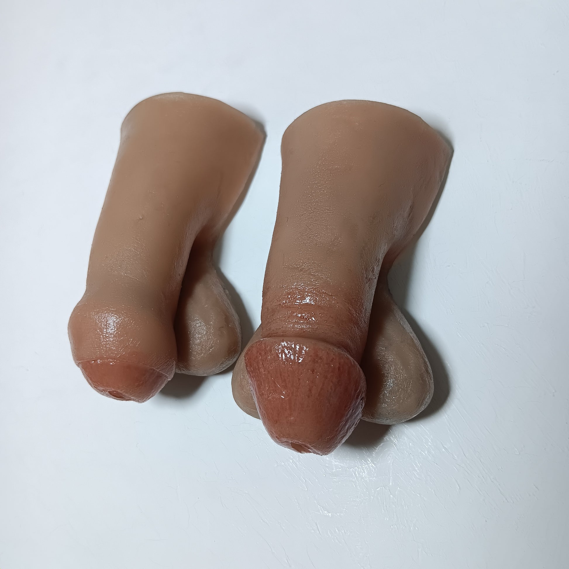 A photo showing two realistic finished 2 inch STP Skins with style options circumcised and uncircumcised lifelike silicone prosthetic.