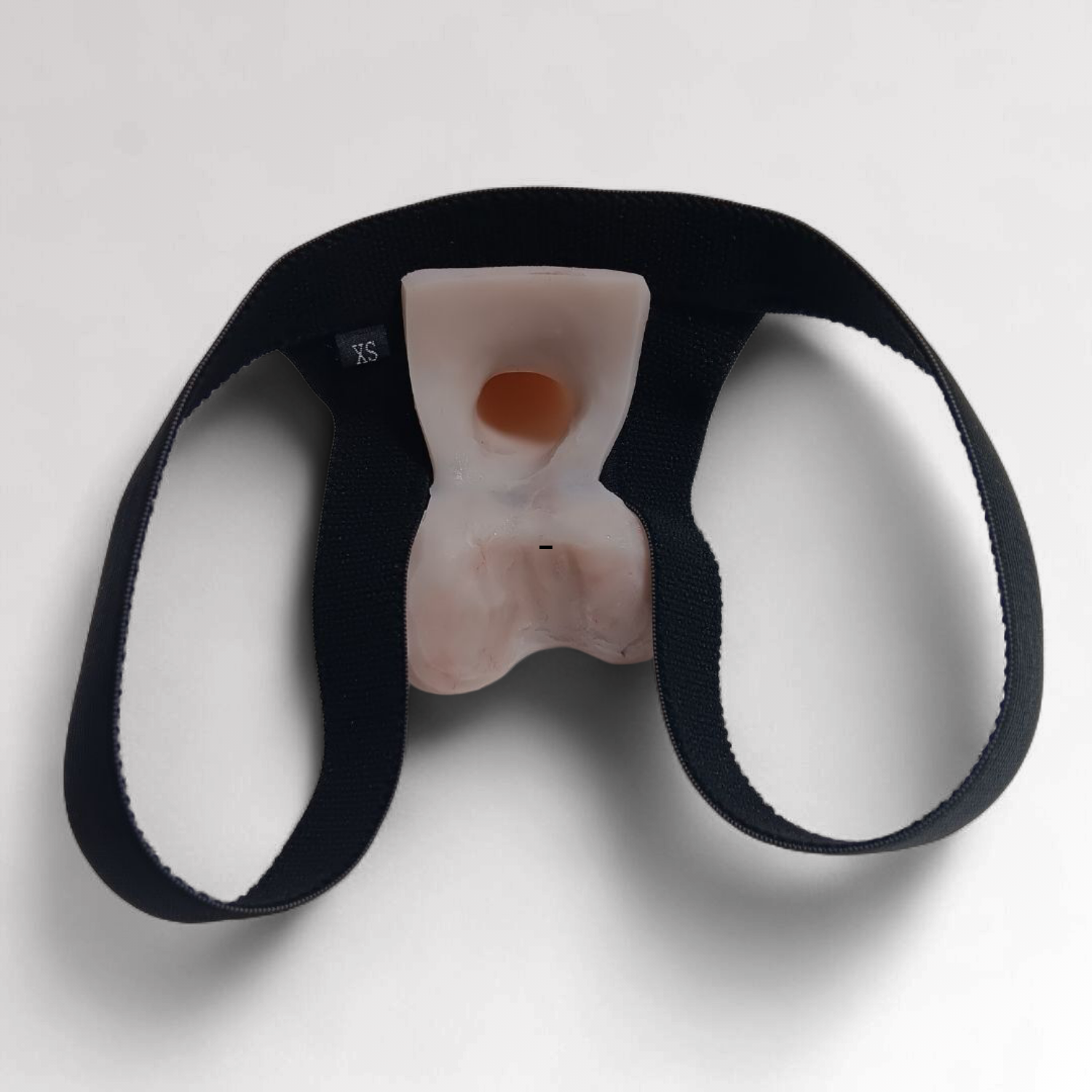 Image of an Action toy in a black Slingshot Harness. Showing from the back side, how the harness has a loop for each leg and the inside of the suction base, featuring the suction hole for wearers sensation and connection to the prosthetic.  