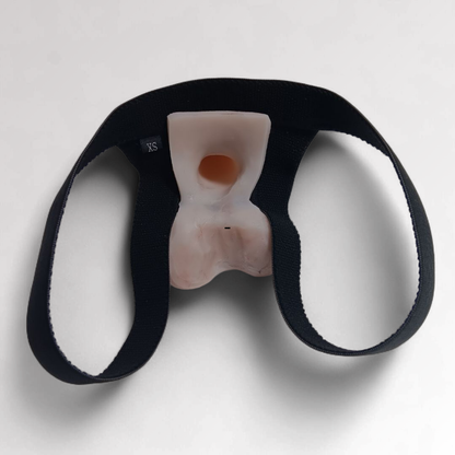 Image of an Action toy in a black Slingshot Harness. Showing from the back side, how the harness has a loop for each leg and the inside of the suction base, featuring the suction hole for wearers sensation and connection to the prosthetic.  
