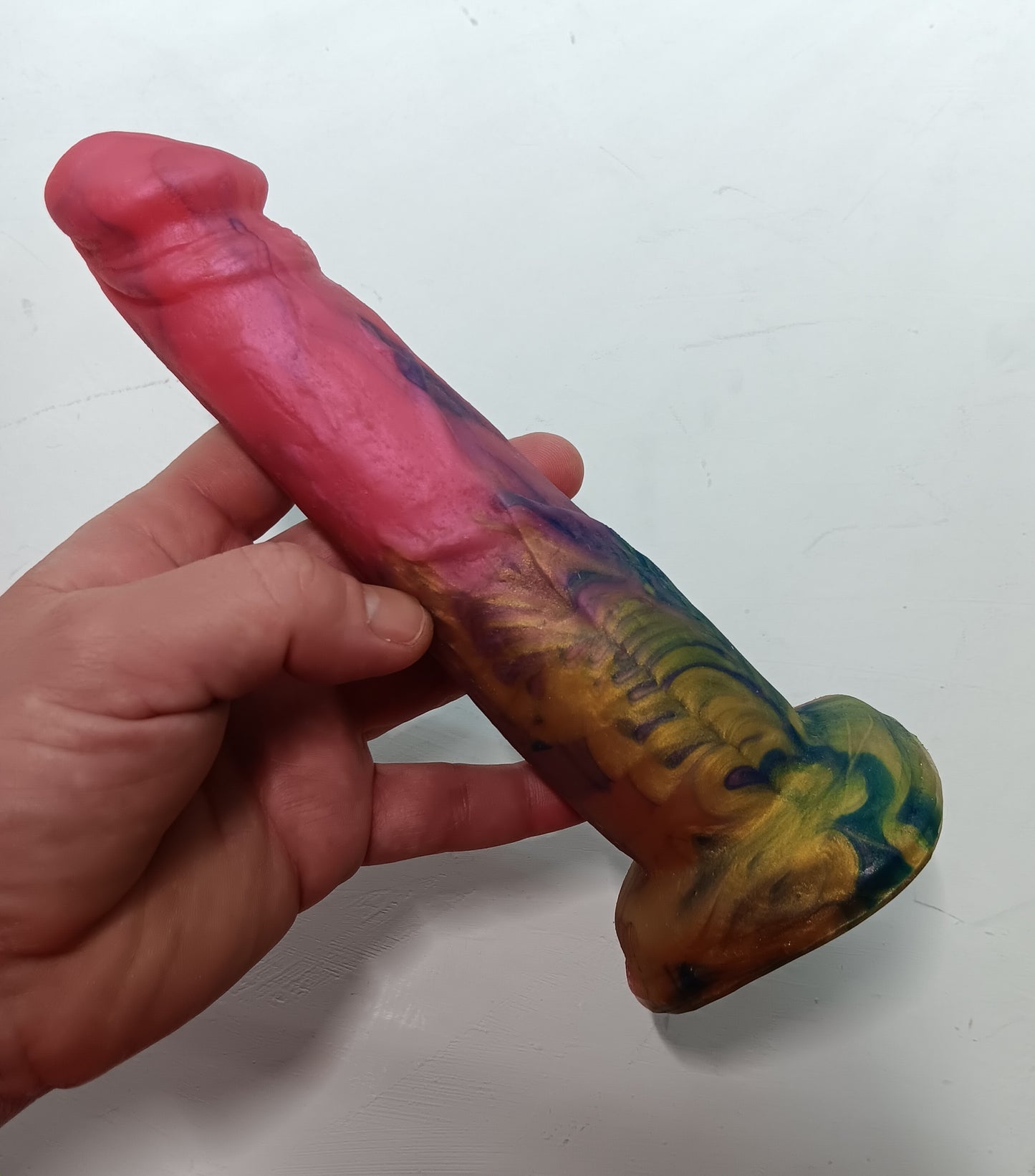 Side view of beautiful bright pink, gold and dark blue swirly platinum silicone B.J. dildo