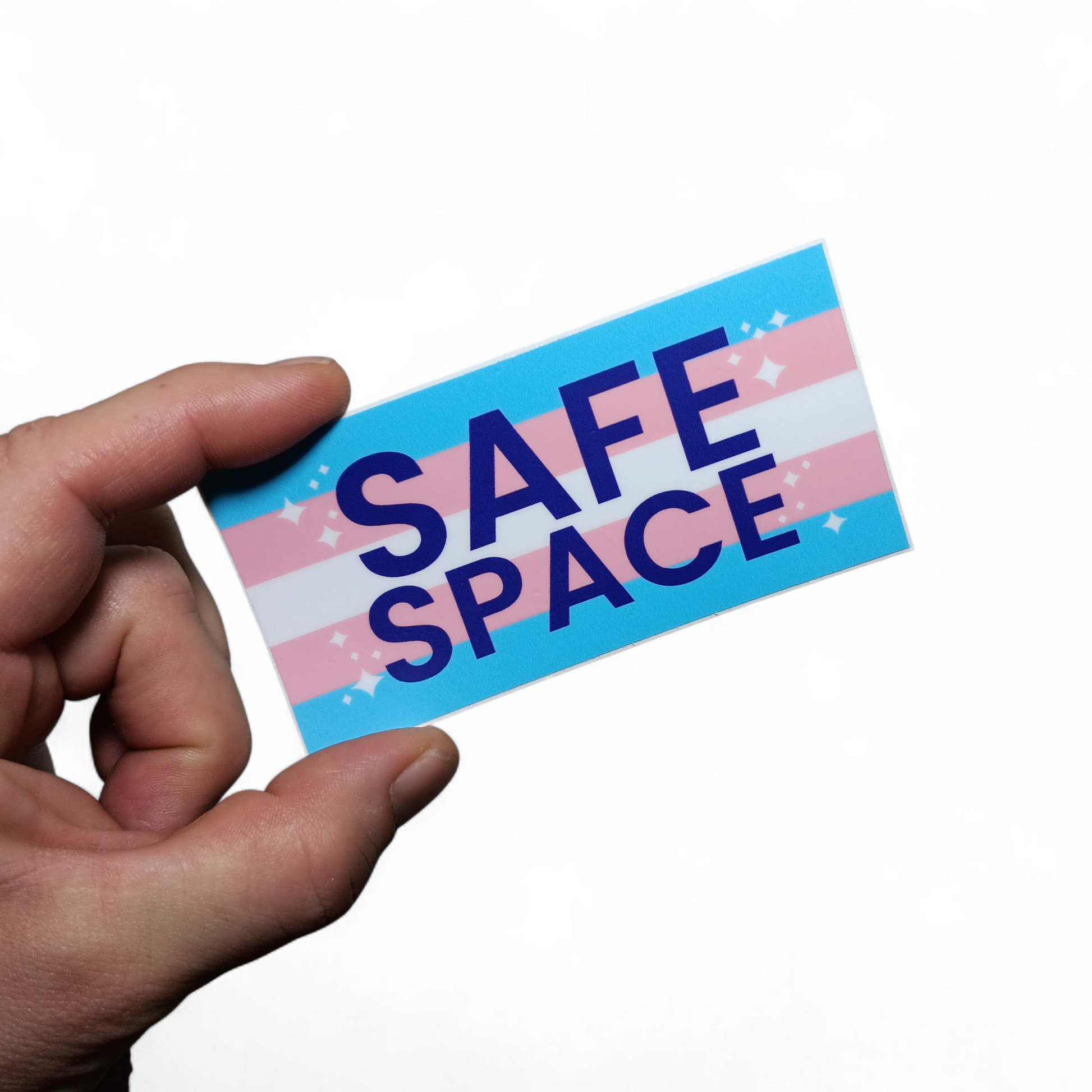 Hand holding a 2 inch x 4 inch sticker that is the trans flag with Safe Space in purple letters.